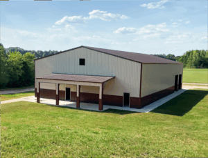 Modern commercial metal building with beige and brown vertical siding, gable roof, and multiple access doors, set on a concrete foundation in a spacious grassy field—ideal for storage, agricultural, or industrial use.