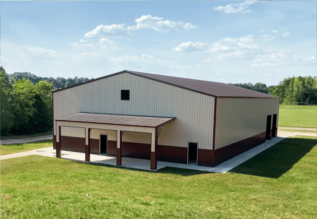 Modern commercial metal building with beige and brown vertical siding, gable roof, and multiple access doors, set on a concrete foundation in a spacious grassy field—ideal for storage, agricultural, or industrial use.